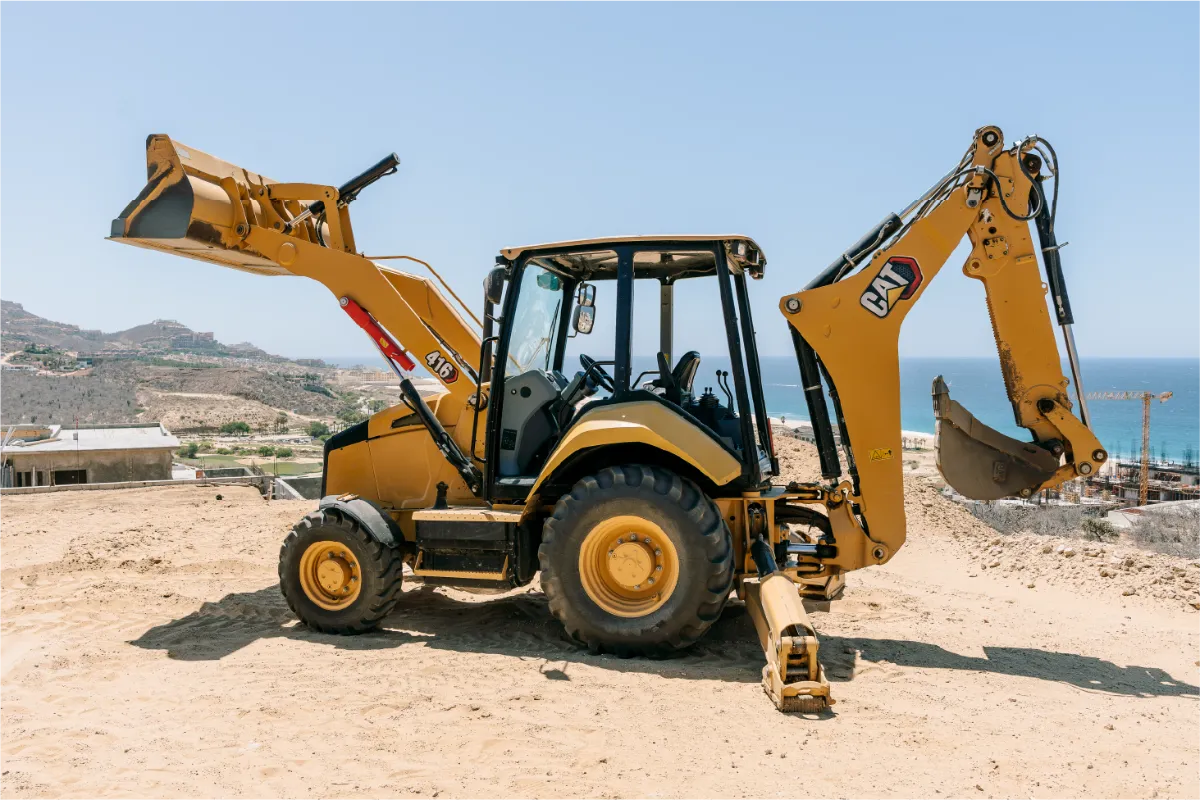 Side view of the CAT 416 backhoe loader, front bucket lifted and rear digging arm raised on a hilltop lot