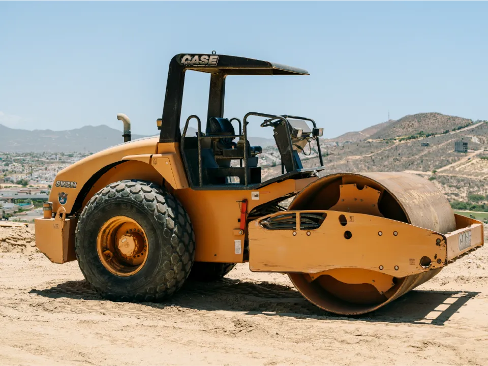 CASE single drum roller compactor on a dirt lot, with hills and houses in the distance