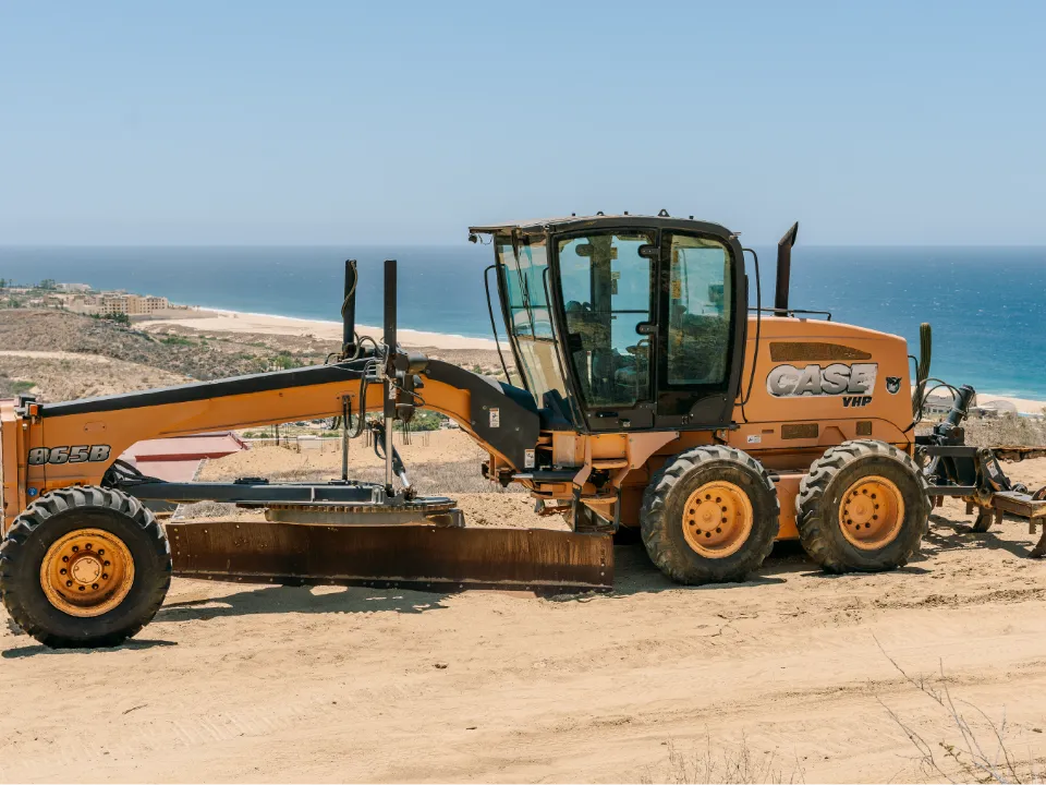 CASE 865B motor grader with its blade lowered on a hilltop site overlooking the coast