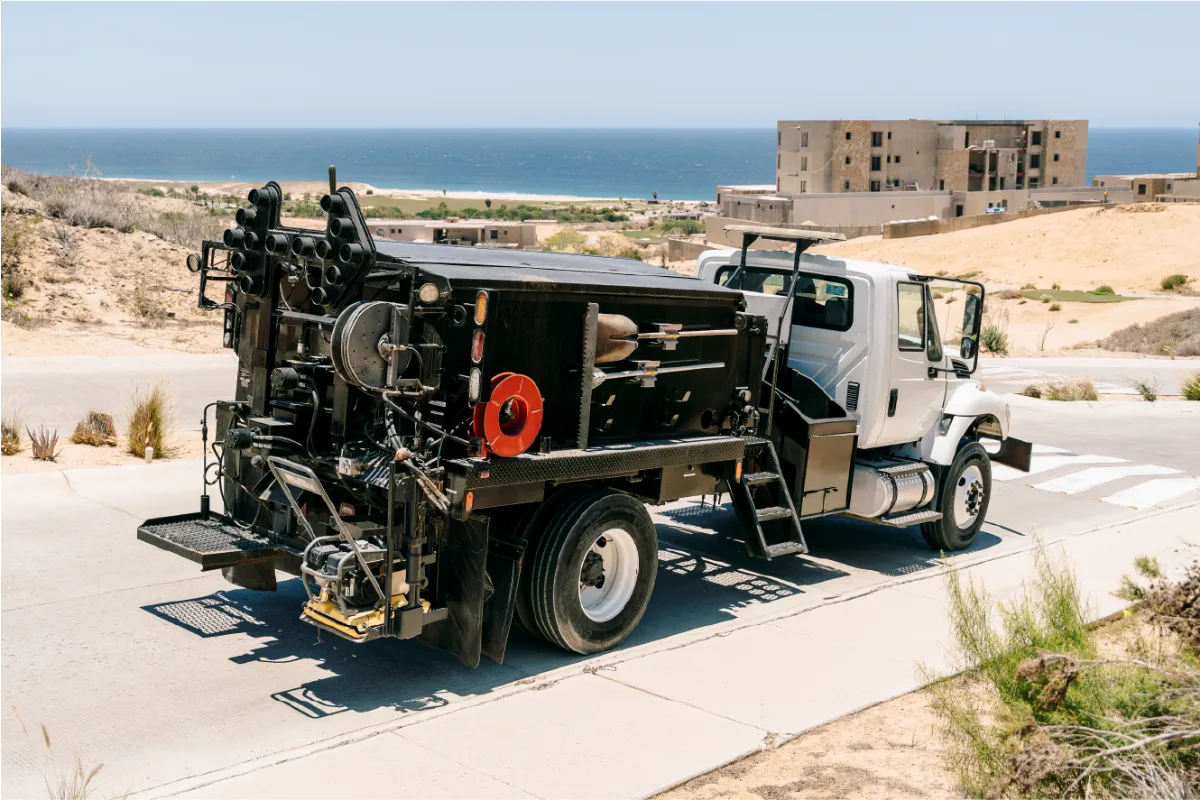 Black Pro Patch 4000 patching body on a white International truck, parked on a paved street above the ocean with its arrow board lights and hose reels at the back