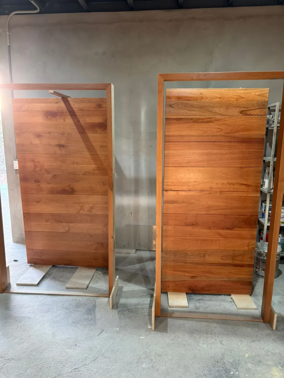 Two solid wood door slabs in wood frames leaning against a bare concrete wall inside a building under construction