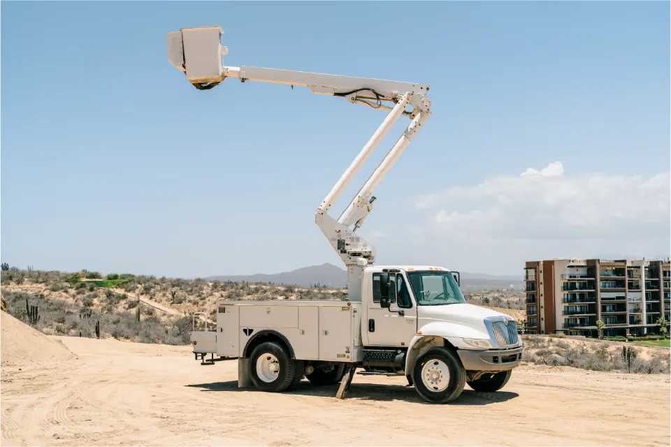 White International 4300 truck with its boom extended and the work basket high in the air, parked on a graded lot near a condominium building
