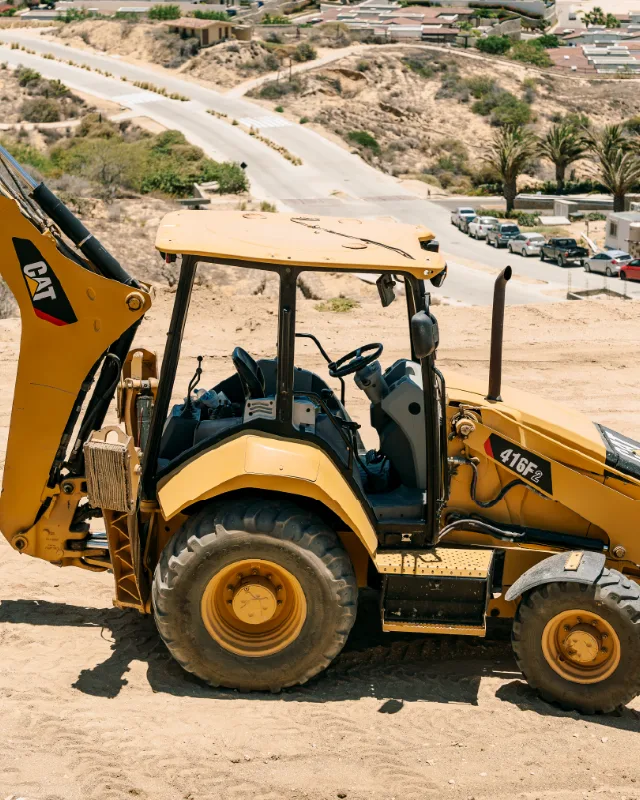 Retroexcavadora CAT trabajando en un terreno en ladera sobre una colonia de Los Cabos