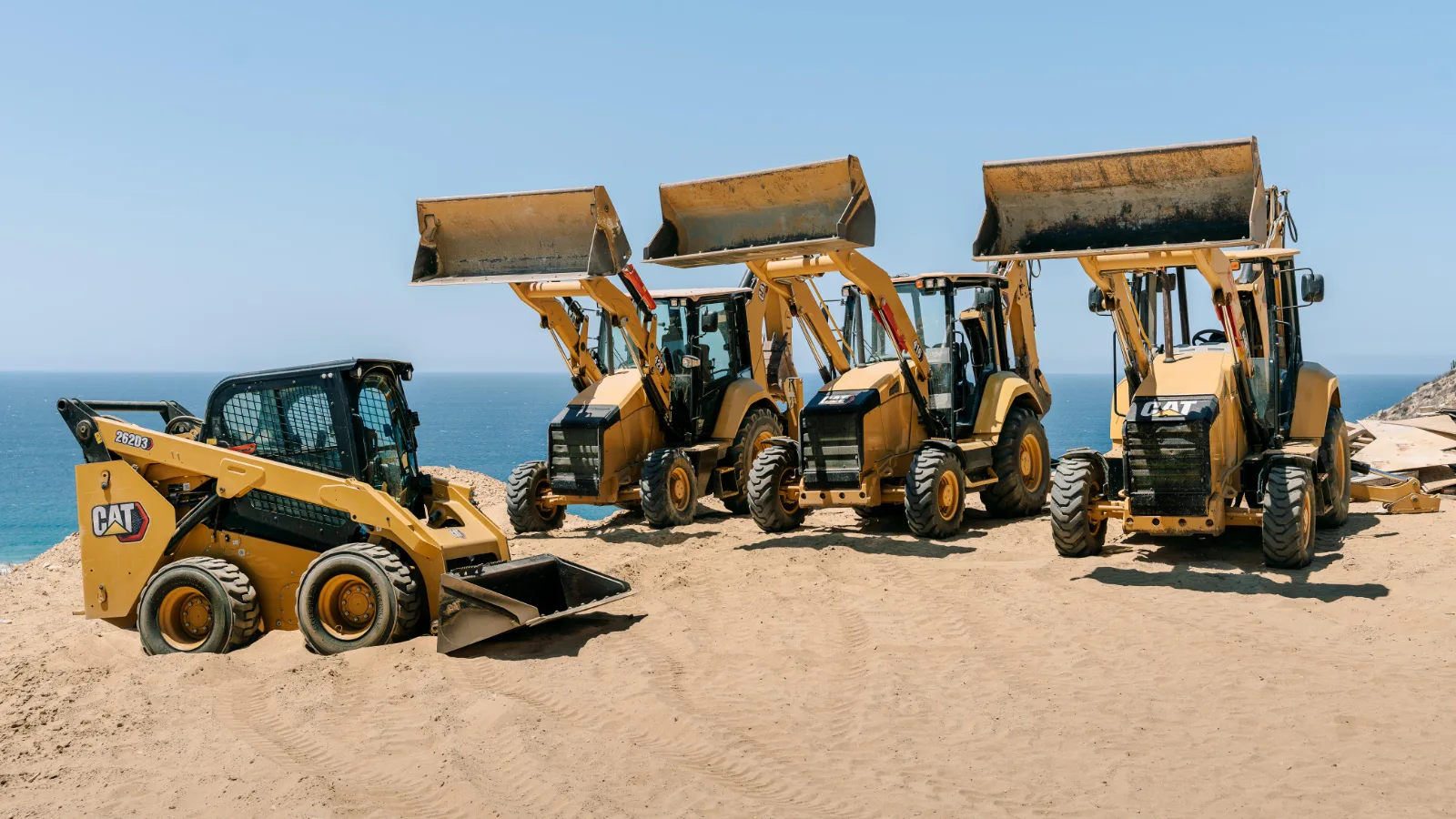 Flotilla de Creatio Construction con retroexcavadoras CAT y un minicargador alineados en una playa de Los Cabos