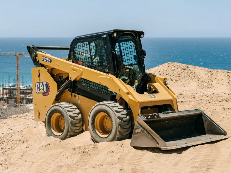Minicargador CAT en un terreno arenoso sobre el mar