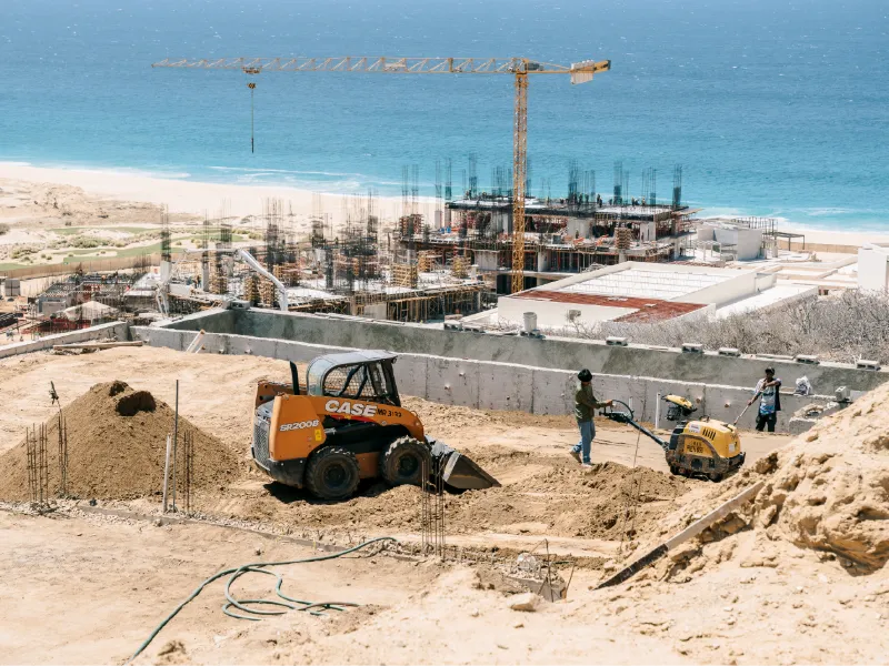 Minicargador y cuadrilla trabajando en una obra frente al mar con una grúa torre